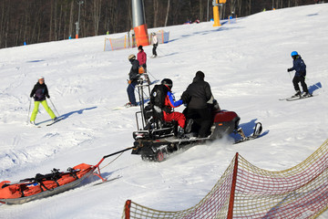 Ratownicy medyczni na skuterze śnieżnym jadą po stoku narciarskim.