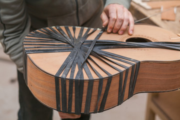 Serious professional guitar-maker working with unfinished guitar at workshop