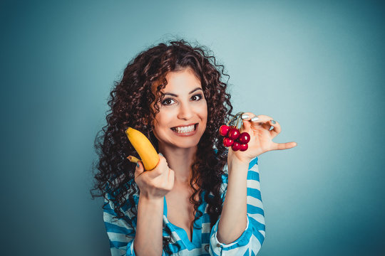Closeup beautiful woman showing giving choosing to eat banana or cherry fruits isolated blue background wall. Healthy lifestyle concept