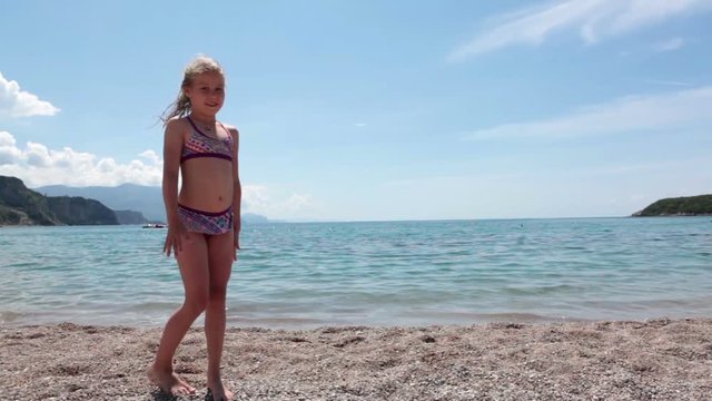 Little Caucasian girl showing gymnastic exercises cartwheel on a sandy beach near the sea