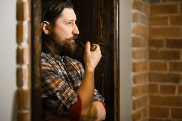 bearded man smoking a pipe in hipster plaid shirt