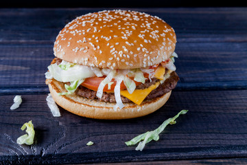 Fresh homemade beef double cheeseburger with cheese, vegetables, tomatoes, salad lettuce, onion and spicy tomato sauce on rustic wooden board, black background. Fast food.

