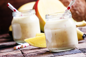 Banana mango smoothie with coconut in a glass jar, vintage woode