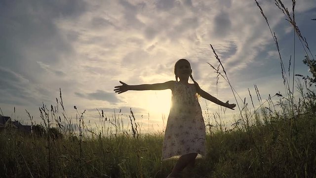One little girl dancing in the field at the sunset time. Kid having fun outdoors. Concept of happy life.