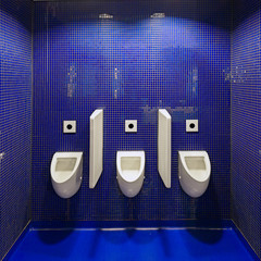 Three white urinals in men public toilet against blue wall.