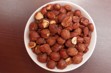 Hazelnuts in white bowl or cup  at wooden background, top view.