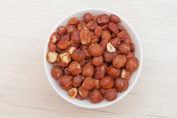 Hazelnuts in white bowl or cup  at wooden background, top view.