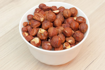 Hazelnuts in white bowl or cup  at wooden background. Healthy fo