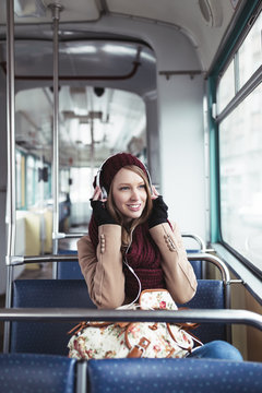 Beautiful young woman sitting in tram, listening to music and looking through window. 
