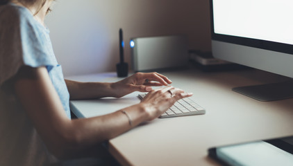 Businesswomen working at office with monitor computer, young hipster manager typing on keyboard, closeup finger female hands texting message, work process concept in workspace, night atmospheric .