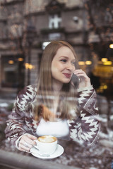 Beautiful woman sitting alone in cafeteria, drinking coffee and talking on cell phone. 