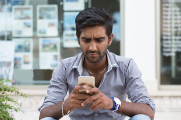 Man phone. Closeup portrait angry indian male holding texting looking at cellphone isolated...