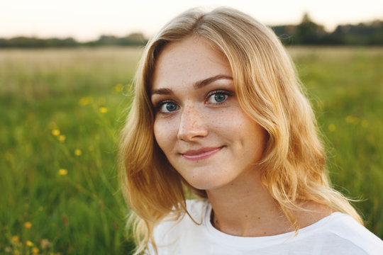 A portrait of beautiful young blue-eyed girl with light hair having charming smile and dimple on her face looking into camera standing over green background having nice time relaxing outdoor in summer