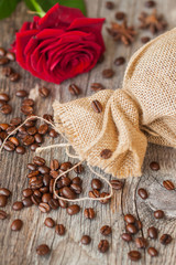 Roasted coffee beans on a brown wooden background with coarse roughly woven burlap and red rose, grunge texture. Top view. Place for your text