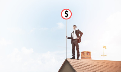 Businessman on house roof showing roadsign with money concept. M