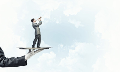 Fototapeta premium Businessman on metal tray playing fife against blue sky background