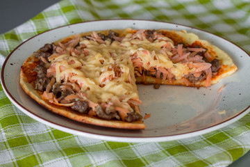 Cutting frittata with tomato sauce, carrot, fried minced beef and cheese on white plate on green checkered napkin.