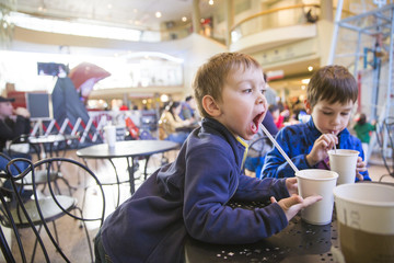  kids in a cafe drinking hot chocolate. funny child drinks of cocoa through a straw