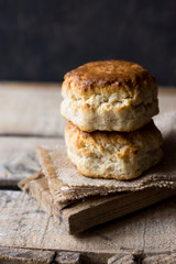 Stack of homemade scones on burlap on vintage wood table, black wall, rustic kitchen interior,...