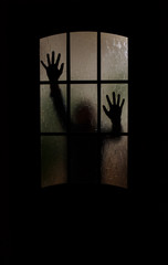 Silhouette of an unknown man with his hands on a door through a closed glass door