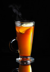 Hot steaming rooibos tea with apple slices on black reflective background