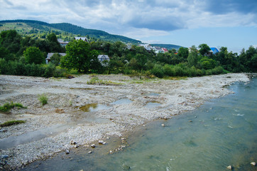 Mountain River in the Carpathians, flows through the village and among beautiful mountains in the afternoon.