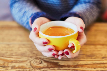 Woman hands with red manicure and cup of fresh hot coffee on wooden table