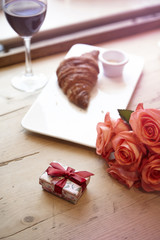 Romantic breakfast for Valentine's Day celebrate concept. Fresh bakery croissant, red wine, rose flowers on wooden table.