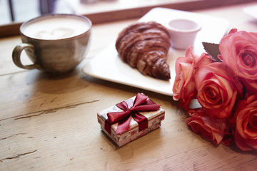 Romantic breakfast for Valentine's Day celebrate. Present box, rose flowers, fresh croissant coffee on wooden table. 