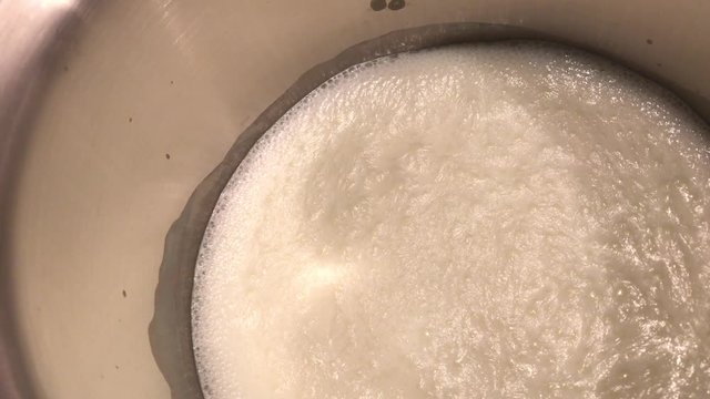 Boiling milk surface in high metal pot 4K 2160p 30fps UltraHD footage - Cream on the top of cooked liquid 3840X2160 UHD video 