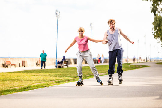 Young couple rollerblading in park holding hands.