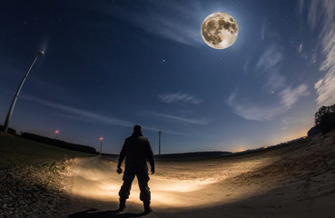 ein Mann steht in der Nacht auf freiem Feld und beobachtet den Mond.