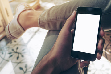 Mockup image of hand holding black mobile phone with blank white screen on thigh with white canvas shoes
