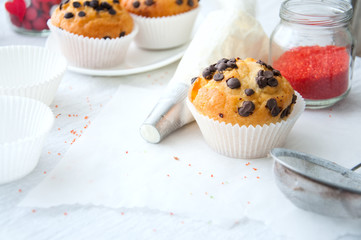Vanilla cupcakes with chocolate chips and whipped cream in pastry bag sprinkled with powdered sugar on the white background