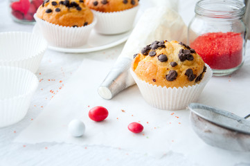 Vanilla cupcakes with chocolate chips and whipped cream in pastry bag sprinkled with powdered sugar on the white background