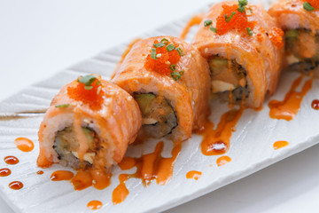 Torched Salmon Maki Sushi with Shrimp Tempura, Avocado and Cheese inside. Topping with Sauce, Ebiko (Shrimp Egg) and Scallion.