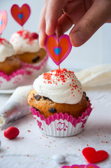 Vanilla cupcakes with chocolate chips and whipped cream frosting sprinkled with red colored sugar on the white background