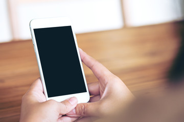 Mockup image of hands holding white mobile phone with blank white screen on vintage wood table in the room