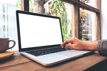 Mockup image of hand using laptop with blank white screen on vintage wooden table in cafe