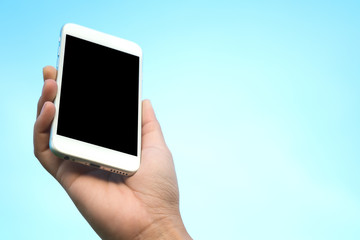 Mockup image of hand holding white mobile phone with blank black screen in blue sky background