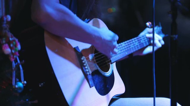Guitarist is holding acoustic guitar near microphone at concert in club