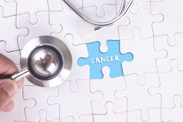 Medical Concept - A doctor holding a Stethoscope on missing puzzle with cancer word