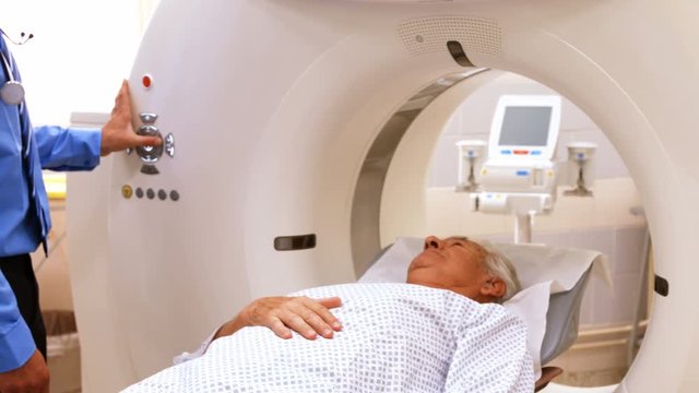 A patient is loaded into an mri machine while doctor and nurse watching