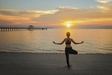 young woman yoga practice on the beach at sunset