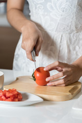 Woman cutting tomato on wood board.
