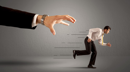 Businessman running away from a huge hand