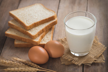 Milk glass with egg and bread on wooden table