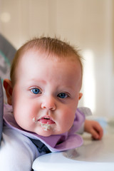 Adorable baby girl gives an expression during her first time being fed baby food
