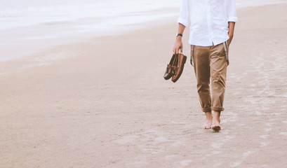 Alone man walking on the beach carrying leather shoes