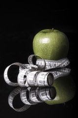 apple and measuring tape on black with reflection